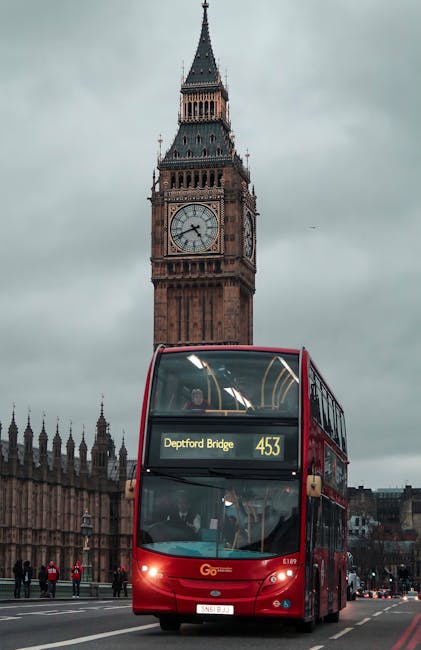 A red double-decker bus approaching on a busy street with several pedestrians nearby, passing in front of the iconic Elizabeth Tower, commonly known as Big Ben, which features a large clock face on it